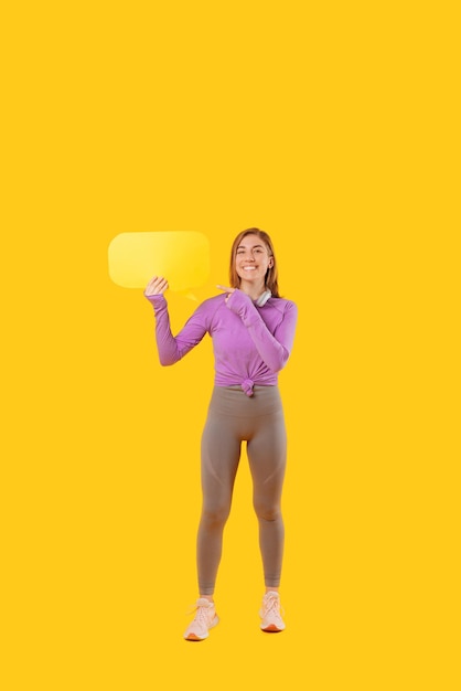 Foto de uma alegre mulher esportiva apontando para o balão amarelo em branco