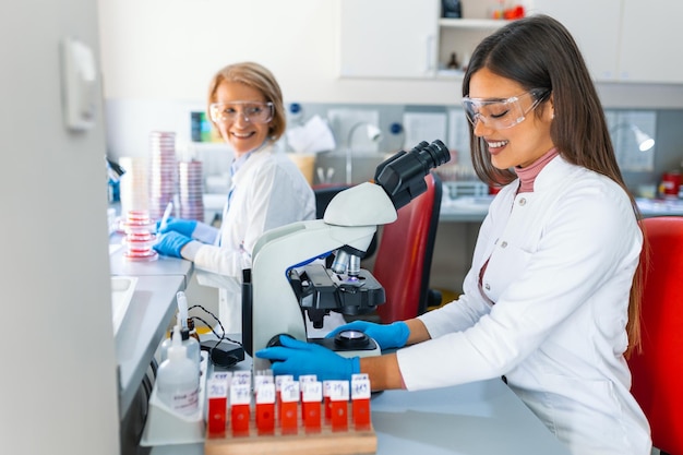 Foto de uma bela cientista feminina olhando para o microscópio mulher microbiologista trabalhando em amostras de moléculas em laboratório moderno com equipamentos tecnológicos