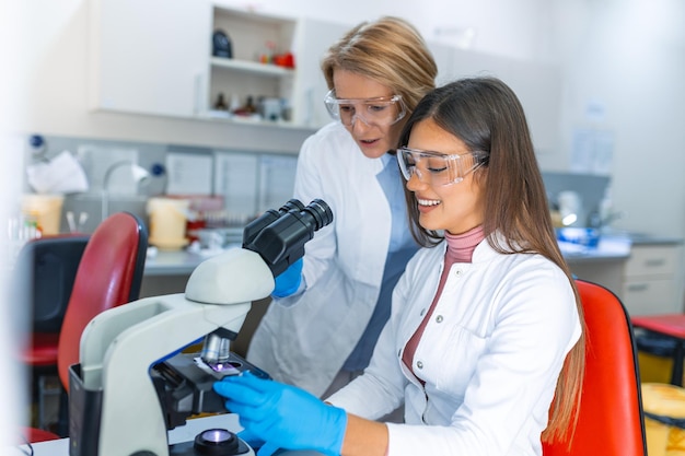 Foto de uma bela cientista feminina olhando para o microscópio mulher microbiologista trabalhando em amostras de moléculas em laboratório moderno com equipamentos tecnológicos