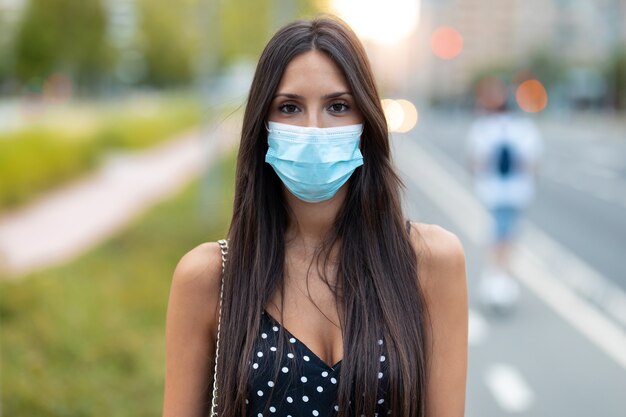 Foto de uma bela jovem em máscara facial em pé na rua, olhando para a câmera.