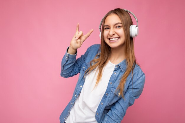 Foto de uma bela jovem loira sorridente, usando fones de ouvido bluetooth sem fio brancos