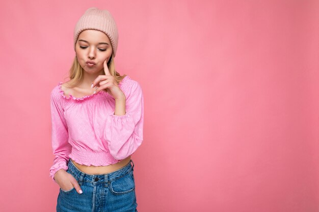 Foto de uma bela jovem loira triste e triste isolada sobre uma parede de fundo rosa usando