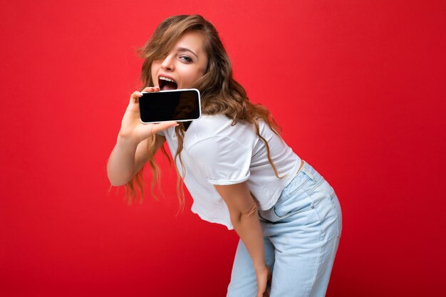 Foto de uma bela jovem sorridente loira bonita vestindo camiseta branca em pé isolado em