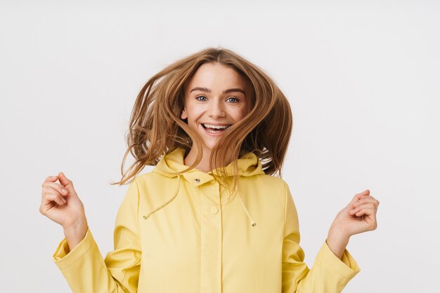 Foto de uma bela mulher alegre em uma capa de chuva, brincando com o cabelo e sorrindo