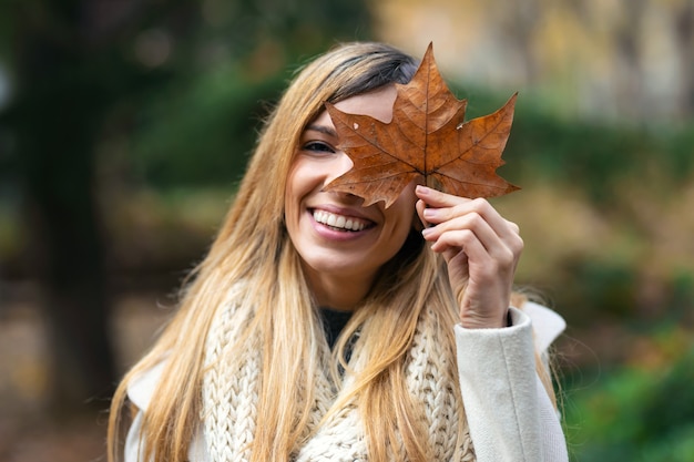 Foto de uma bela mulher sorridente se divertindo com licença enquanto cobre os olhos com ela, olhando para a câmera no parque no outono.