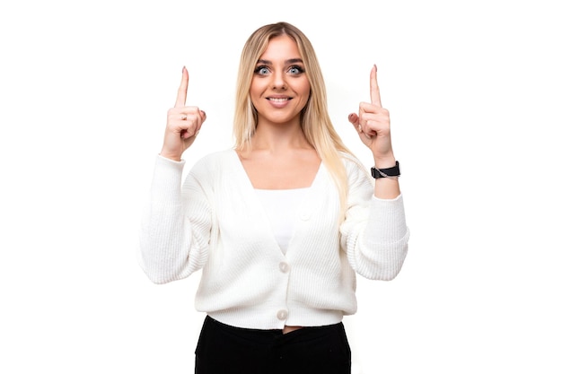 Foto de uma bela positiva feliz sorridente jovem loira com maquiagem em um elegante suéter de malha branca e calça preta mostra os dedos isolados em um fundo branco com espaço vazio para o texto.