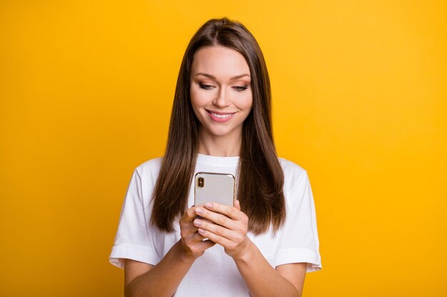 Foto de uma blogueira morena usando o aplicativo no smartphone, sorrindo, isolada em um fundo de cor amarela brilhante