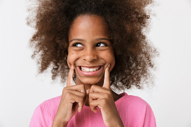 Foto de uma criança feliz sorridente jovem garota africana posando isolado sobre a parede branca.