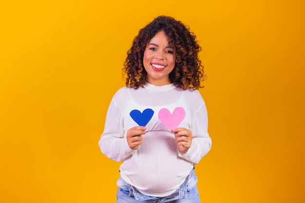 Foto de uma doce mulher esperando criança usar roupa branca apontando a barriga segurando o coração azul rosa isolado fundo amarelo