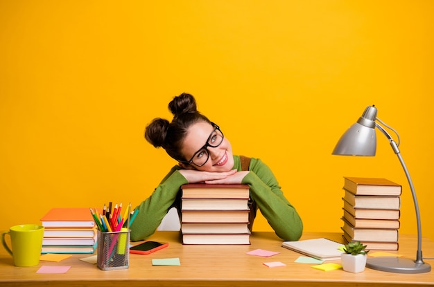 Foto de uma estudante sentada na mesa relaxando em um livro isolado em um fundo amarelo