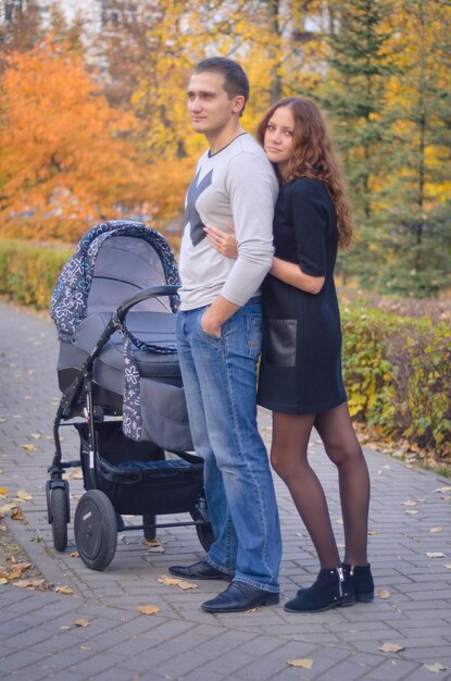 Foto de uma família de três. Família jovem na caminhada com o bebê no carrinho.