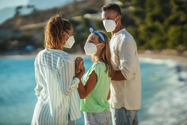 Foto de uma família feliz com máscara protetora N95 passando tempo na praia na pandemia de corona. Eles estão tendo auto-isolamento na natureza.