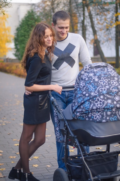 Foto de uma família olhando para seu recém-nascido. Família jovem na caminhada com o bebê no carrinho.