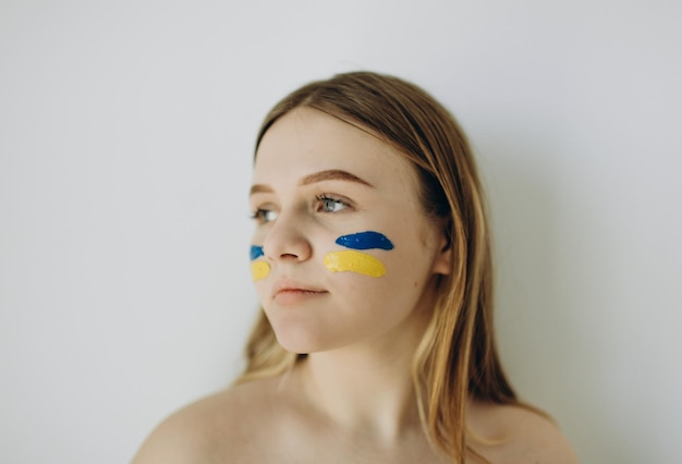 Foto de uma garota contra uma parede branca com uma bandeira da ukrina nas bochechas