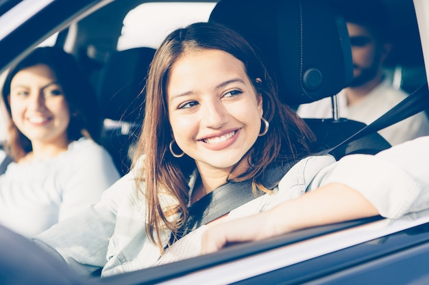 Foto de uma garota feliz dirigindo um carro com os amigos