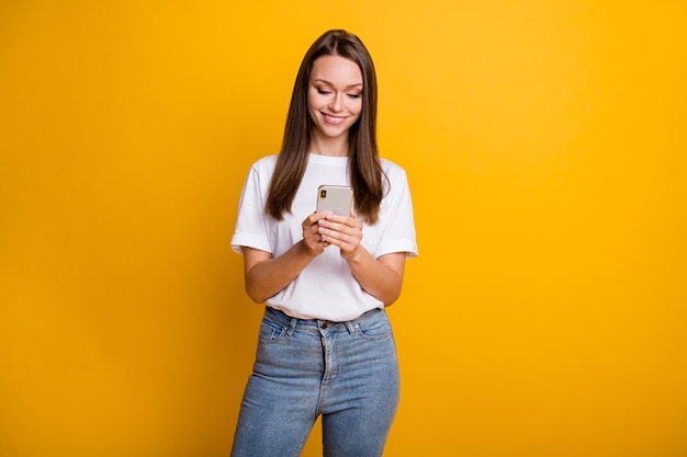 Foto de uma garota influente usando um comentário de mensagem de texto no celular, vestindo uma camiseta jeans isolada em um fundo de cor amarela brilhante