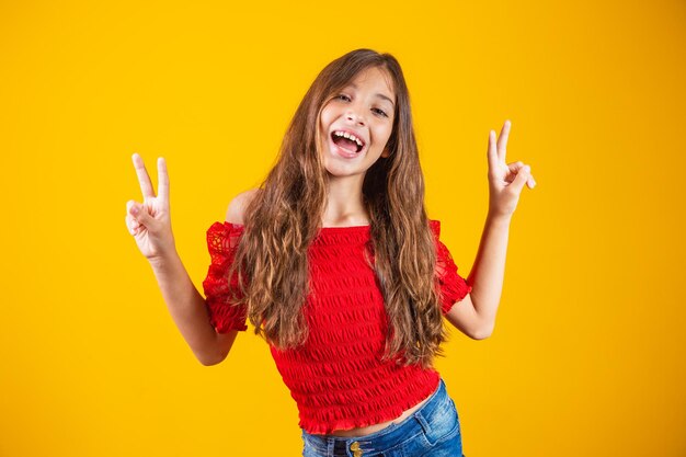 Foto de uma garota pré-adolescente encantadora e delicada fazendo um sinal de V sorrindo isolado em fundo amarelo.