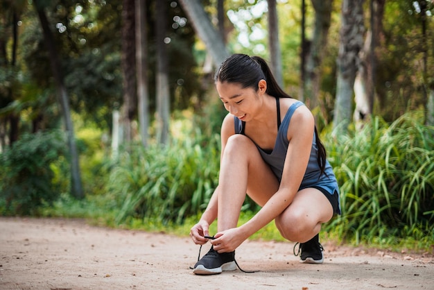 Foto de uma garota sorridente do esporte asiático amarrando os cadarços dos sapatos no parque