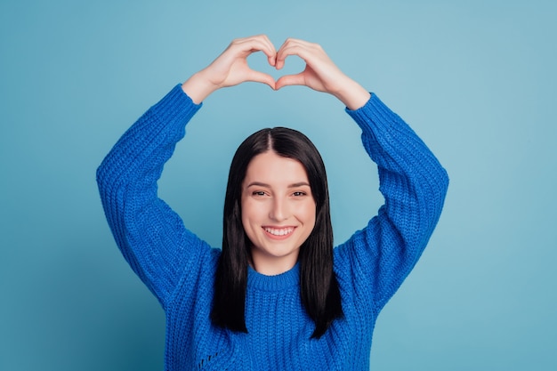 Foto de uma jovem adorável e atraente mostrando a figura do coração, amor, dia dos namorados, isolada sobre o fundo de cor azul