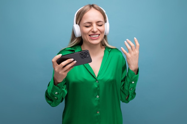 Foto de uma jovem adulta bonita e bem cuidada curtindo música em fones de ouvido em um fundo azul