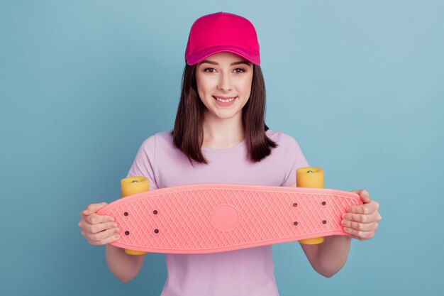 Foto de uma jovem alegre com chapéu segurando longboard skate esportivo isolado turquesa de fundo