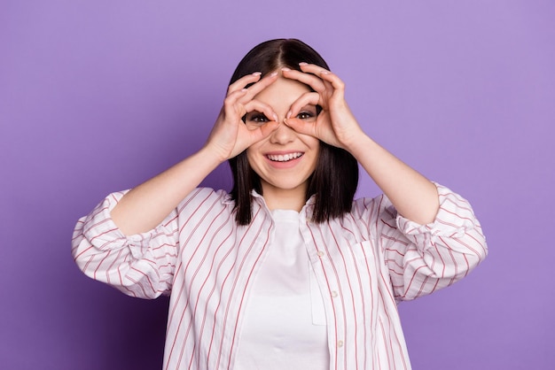 Foto de uma jovem alegre se diverte mostrando óculos de binóculos okey figners isolados sobre fundo de cor violeta