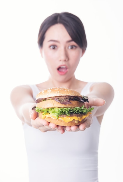 Foto de uma jovem asiática chocada, isolada, comendo um hambúrguer