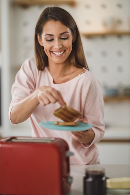 Foto de uma jovem assando um pedaço de torrada na torradeira no café da manhã em casa.