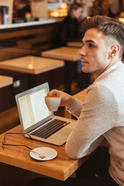 Foto de uma jovem atraente sentada no café e conversando pelo computador portátil. Olhando para o lado.