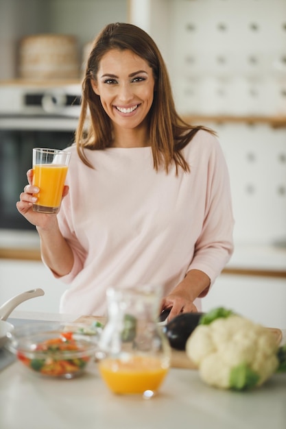 Foto de uma jovem bebendo suco de laranja fresco em sua cozinha.