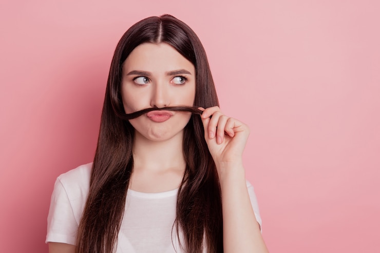 Foto foto de uma jovem brincando com uma careta se divertindo, mostrando um bigode isolado sobre um fundo de cor rosa