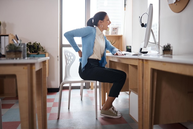 Foto de uma jovem empresária com dor nas costas enquanto trabalhava em sua mesa em um escritório moderno