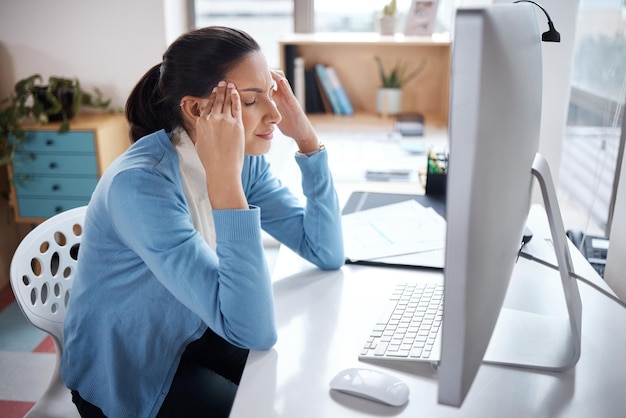 Foto de uma jovem empresária parecendo estressada enquanto usa um laptop em sua mesa em um escritório moderno