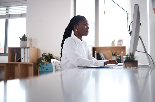 Foto de uma jovem empresária usando um computador em sua mesa em um escritório moderno