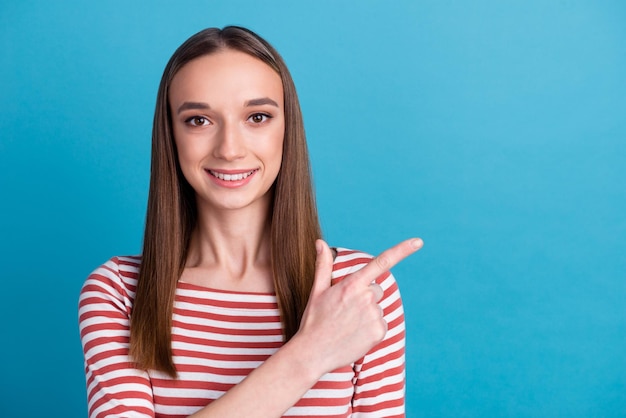 Foto de uma jovem encantadora e doce camisa vestida sorrindo apontando o dedo vazio isolado fundo de cor azul