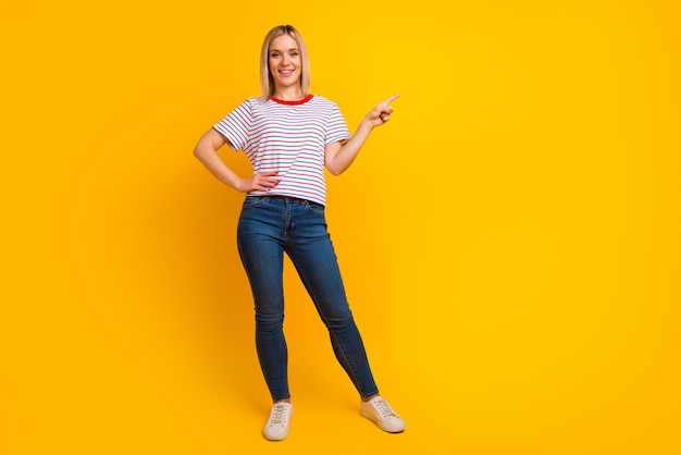 Foto de uma jovem encantadora e doce camisa vestida sorrindo apontando o espaço vazio do dedo isolado fundo amarelo