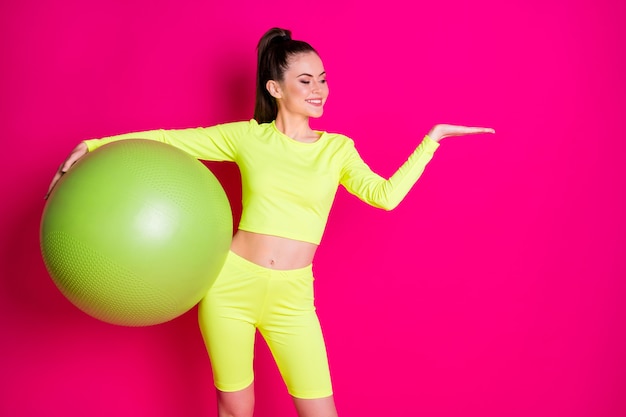 Foto de uma jovem esportista positiva segurar apto bola mão presente espaço vazio isolado sobre fundo de cor rosa brilhante