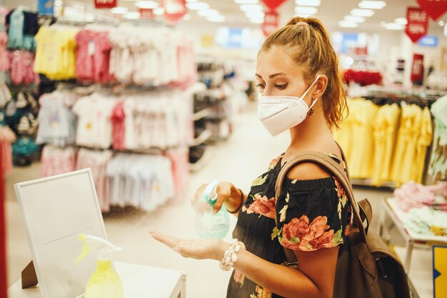 Foto de uma jovem está usando máscara protetora N95 e usando spray anti-séptico para desinfetar as mãos enquanto compra no supermercado durante a pandemia de Covid-19.