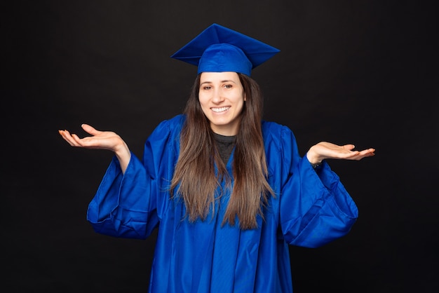 Foto de uma jovem estudante com túnica azul e chapéu de formatura fazendo gesto de não sei