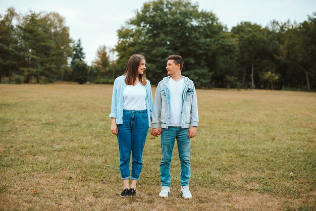 Foto de uma jovem família em pé no parque de mãos dadas e olhando uns para os outros