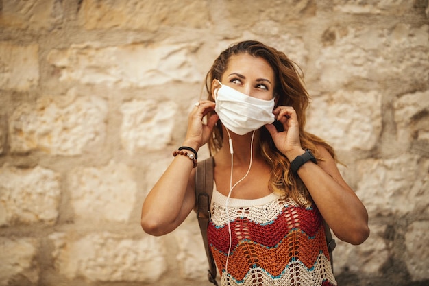 Foto de uma jovem feliz com máscara protetora passando tempo de férias e se divertindo durante a exploração de uma cidade mediterrânea na pandemia de corona.