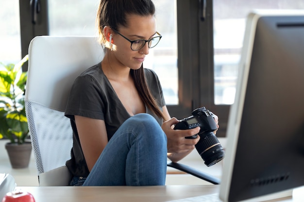 Foto de uma jovem fotógrafa profissional revisando as fotos que tirou com a câmera enquanto estava sentada no estúdio.