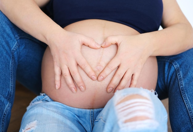 Foto de uma jovem grávida tocando a barriga e mostrando o símbolo do coração