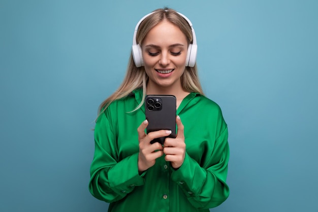 Foto de uma jovem loira bonita e atraente em fones de ouvido com um smartphone nas mãos em um azul