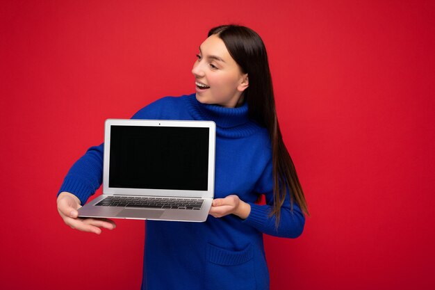 Foto de uma jovem morena bonita muito feliz segurando um laptop e olhando para o lado