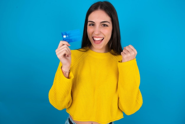 Foto foto de uma jovem morena impressionada e sortuda com o punho do braço segurando o cartão de crédito celebrado