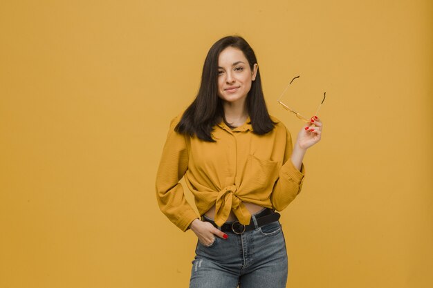 Foto de uma jovem mulher com óculos de sol e parece tão feliz. Veste camisa amarela, fundo de cor amarela isolado.