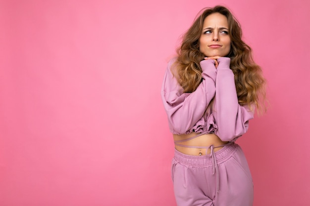 Foto de uma jovem mulher loira muito pensativa e emocional usando um capuz rosa isolado no rosa