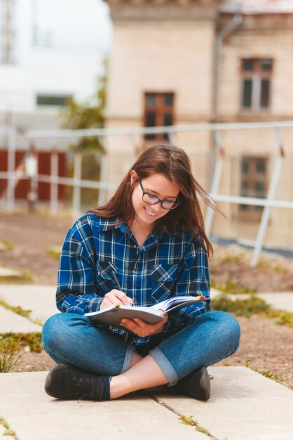 Foto de uma jovem sentada ao ar livre na cidade e fazendo anotações na agenda