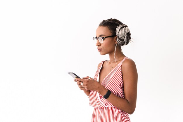 Foto de uma jovem séria com dreads posando isolado no branco, usando bate-papo do telefone móvel.